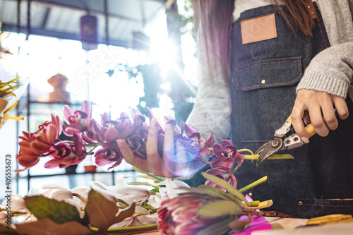 Florist at work: pretty young woman making fashion modern bouquet of different flowers. Smiling lovely young woman florist arranging plants in flower shop