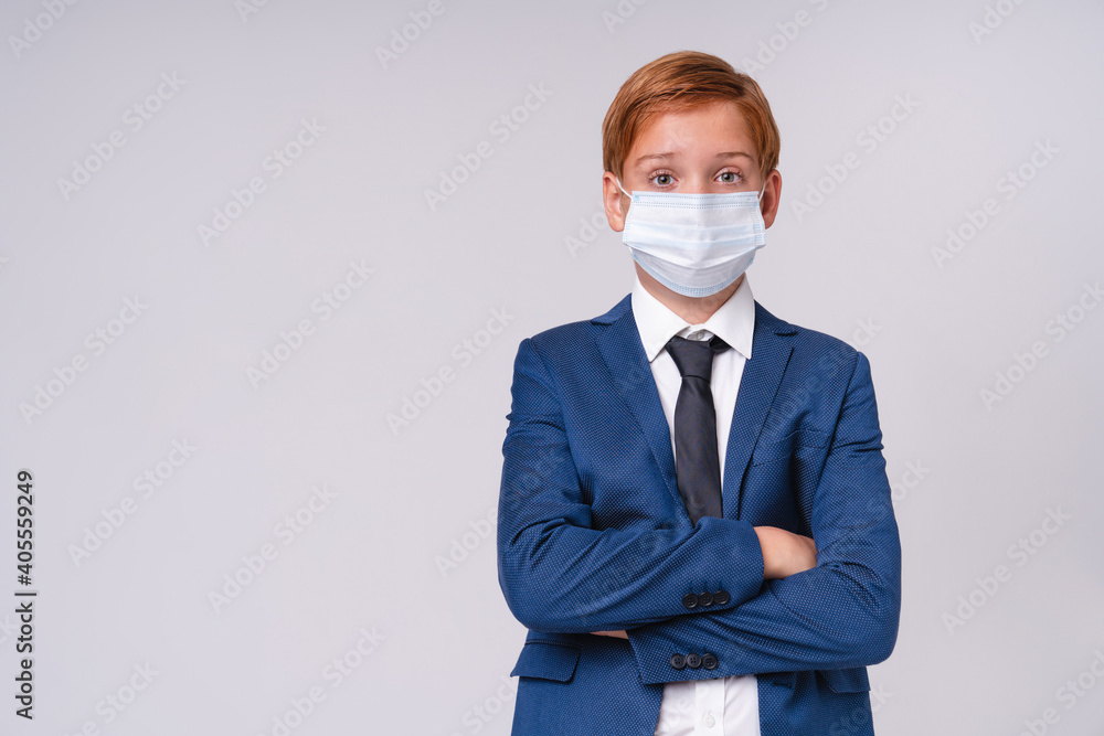 Serious redhead preteen boy in formal outfit wearing medical mask against Covid 19 standing with his arms crossed isolated over grey background Serious redhead preteen boy in formal outfit wearing medical mask against Covid 19 standing with his arms crossed isolated over grey background