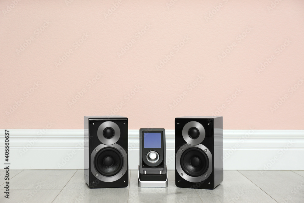 Modern powerful audio speakers and remote on floor near pink wall. Space for text Modern powerful audio speakers and remote on floor near pink wall. Space for text