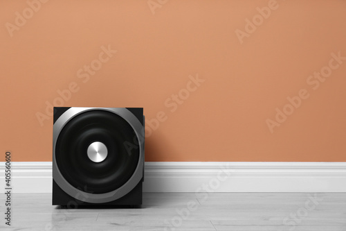Modern powerful subwoofer on floor near orange wall, space for text. Audio speaker system photo
