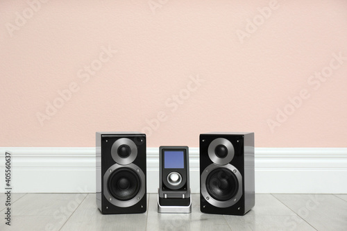 Modern powerful audio speakers and remote on floor near pink wall. Space for text