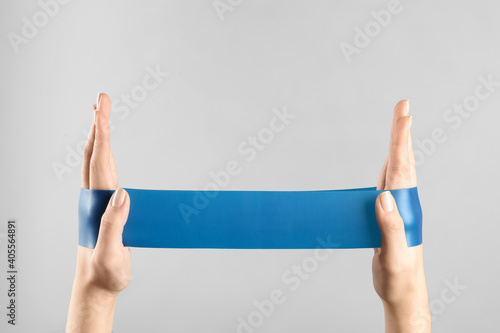 Woman with fitness elastic band on light grey background, closeup photo