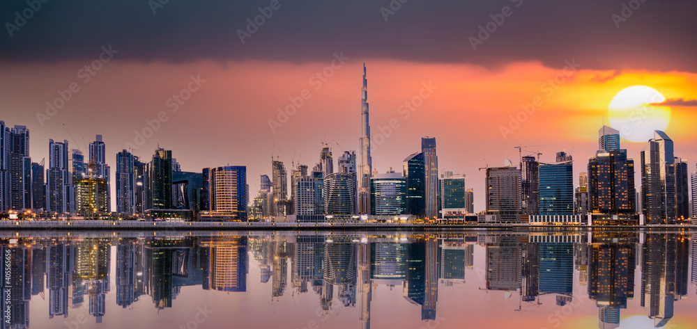 Panoramic view of the Dubai skyline at sunset with buildings and skyscrapers reflected on the river flowing in the foreground. Dubai, UAE.