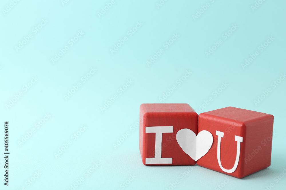 Phrase I Love You made of paper letters and heart connecting two red cubes on light blue background Phrase I Love You made of paper letters and heart connecting two red cubes on light blue background