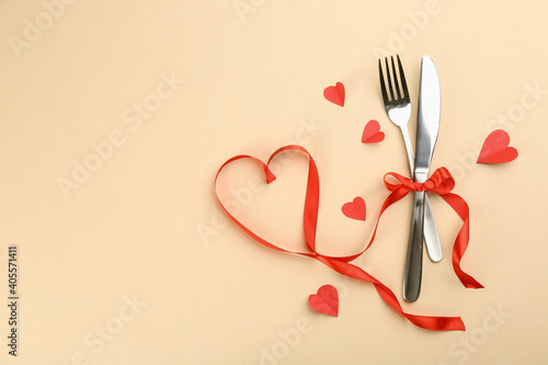 Beautiful cutlery set, hearts and red ribbon on beige background, flat lay with space for text. Valentine's Day dinner