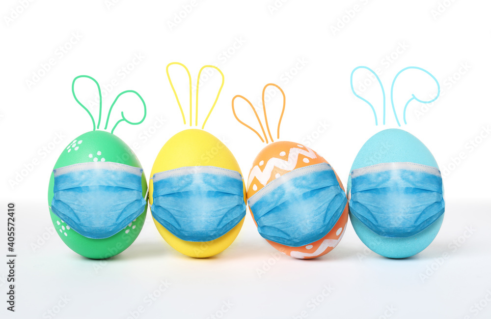 COVID-19 pandemic. Colorful Easter eggs with cute bunny ears in protective masks on white background COVID-19 pandemic. Colorful Easter eggs with cute bunny ears in protective masks on white background
