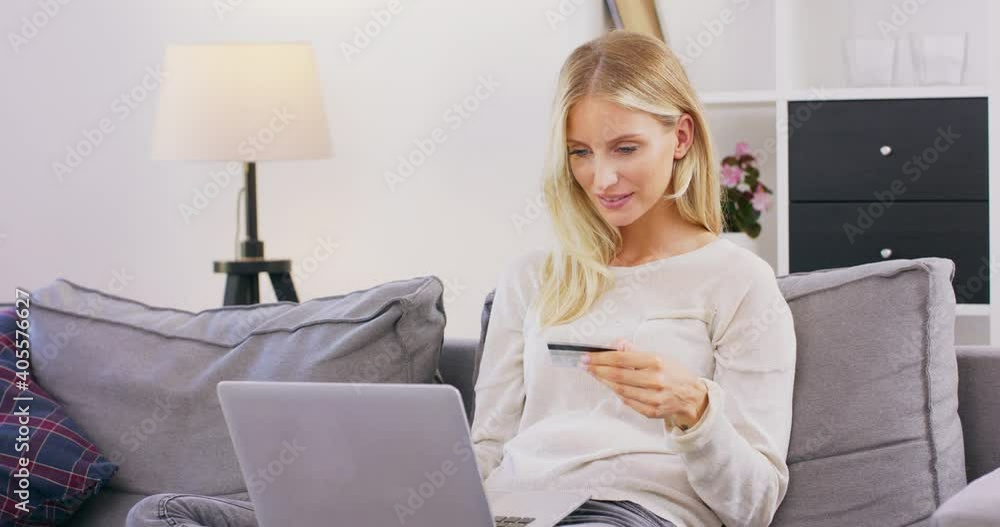 Smiling and happy woman sitting on sofa in living room shopping online on laptop. Pretty caucasian middle-aged girl spending money from credit card during online shopping. Smiling and happy woman sitting on sofa in living room shopping online on laptop. Pretty caucasian middle-aged girl spending money from credit card during online shopping.
