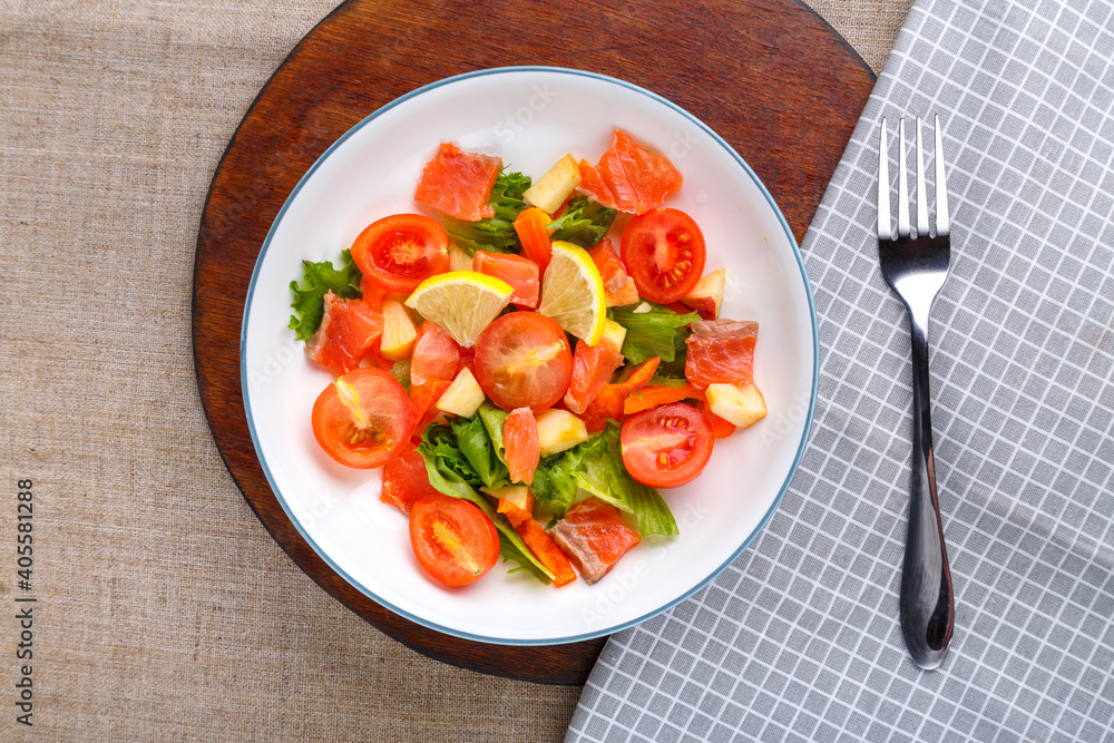 Salad with cold salmon and cherry tomatoes in a plate on a gray background on a wooden stand a stand next to a fork. Salad with cold salmon and cherry tomatoes in a plate on a gray background on a wooden stand a stand next to a fork.