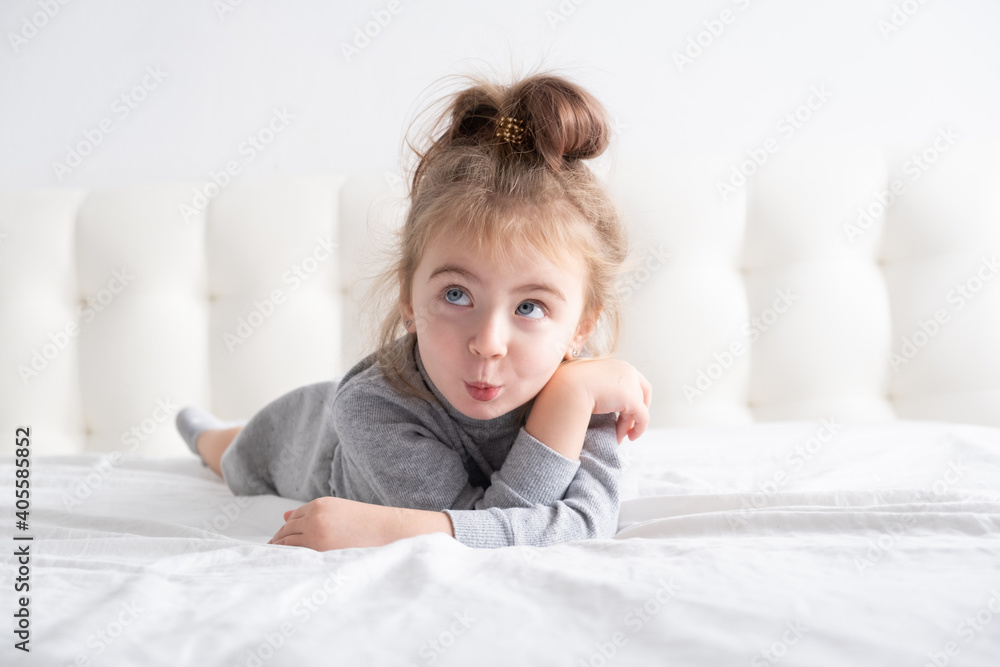 little girl in grey turtleneck having fun on white bedding little girl in grey turtleneck having fun on white bedding