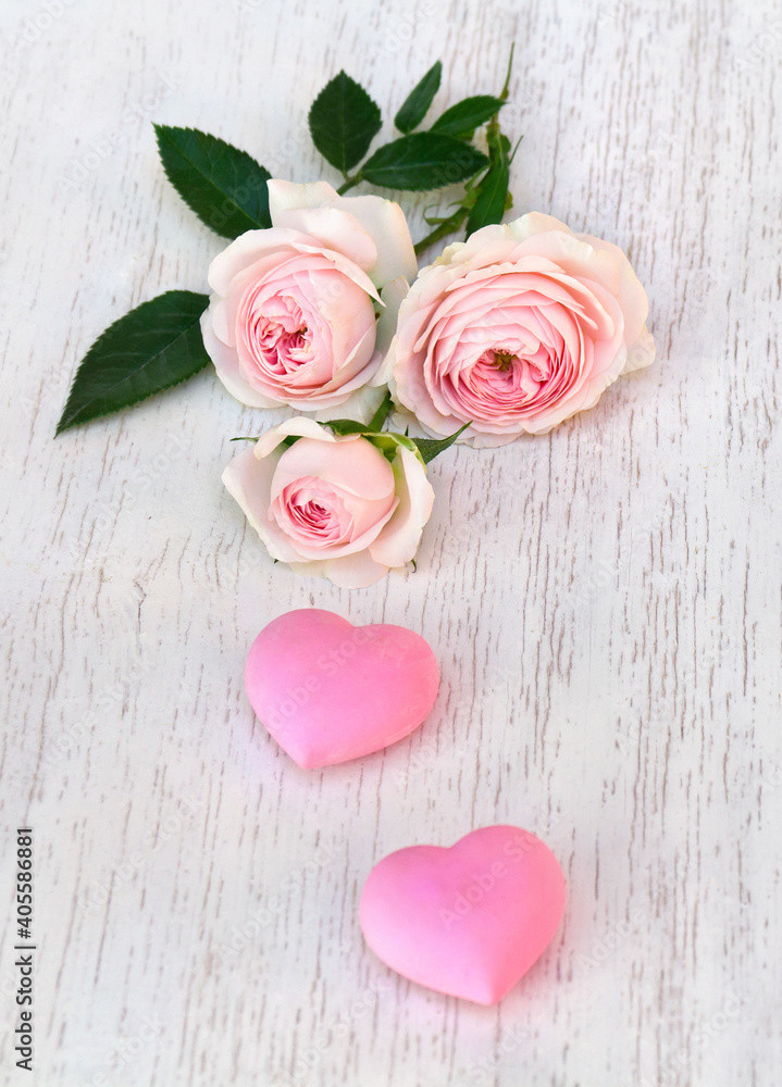 Fototapeta premium Flowers pink roses with pink hearts on background of white painted wooden table with space for text. Decoration of Valentine Day