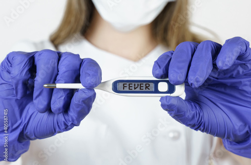 The doctor holds a thermometer in his hands  on the electronic screen of which it is written - FEVER