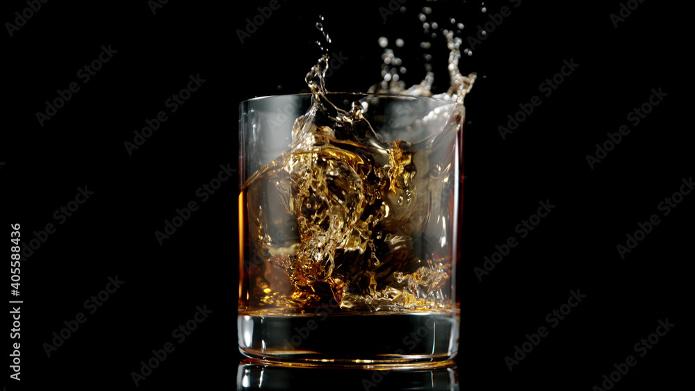 Glass of whisky with splashing liquid and ice rocks inside. Glass of whisky with splashing liquid and ice rocks inside.