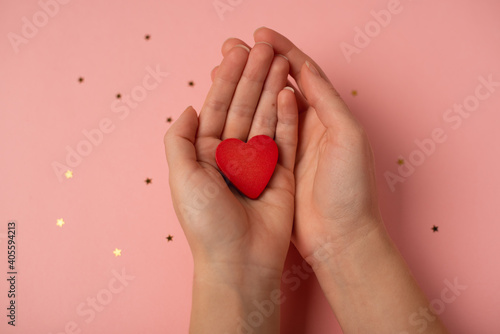 Woman's hands holding a red wooden heart on a rose background. The concept of Valentine's day.
