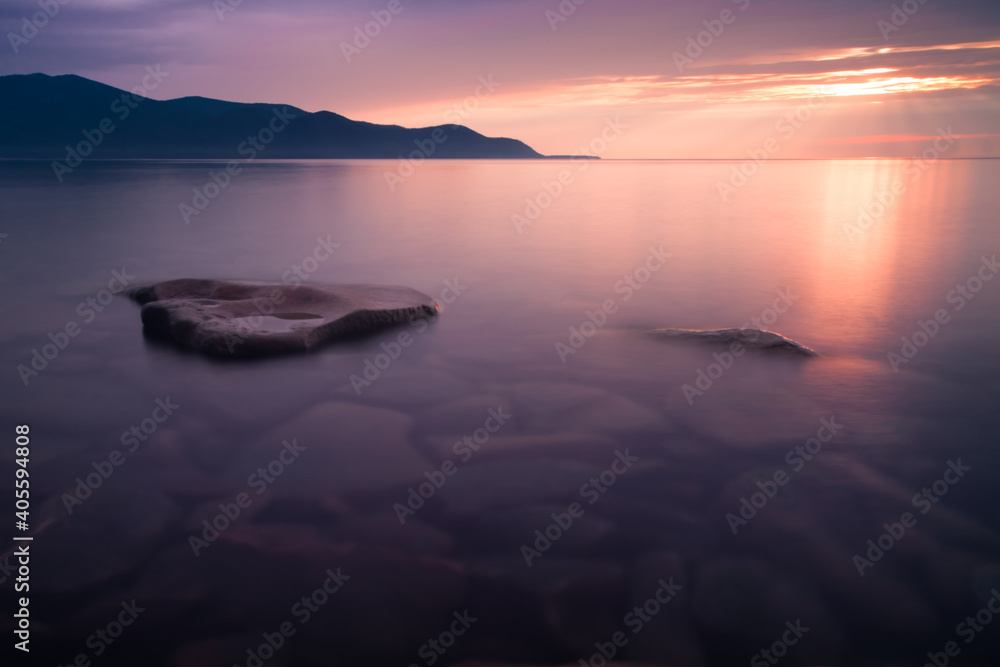 Pink sunset - clear water of Baikal. Kanmni mountains in the distance