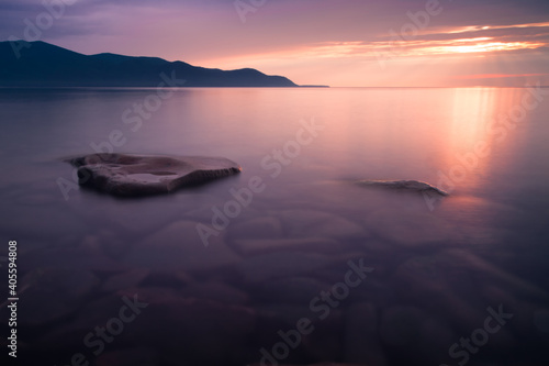 Pink sunset - clear water of Baikal. Kanmni mountains in the distance