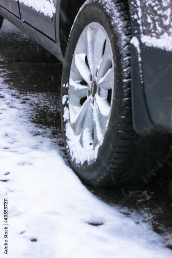A new car wheel with a rubber tire close up covered with white snow in a snowfall, dangerous weather conditions for long car trips, winter tires.