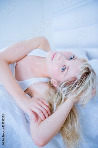 Young, slender woman poses on a bed in white cotton linen