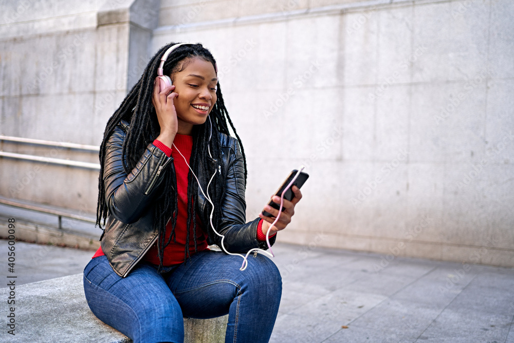 Portrait of a smiling African-American woman with a cell phone is chatting or listening to music on the streets of the city. The hair is braided into dreadlocks.