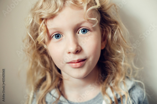 Closeup portrait of beautiful smiling Caucasian blonde girl with long hair on light neutral beige background. Pretty real girl child with natural emotion. Happy authentic childhood lifestyle.