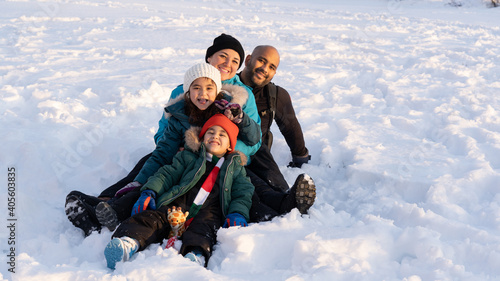 four member interracial family smiling too camera sitting in the snow during sunset