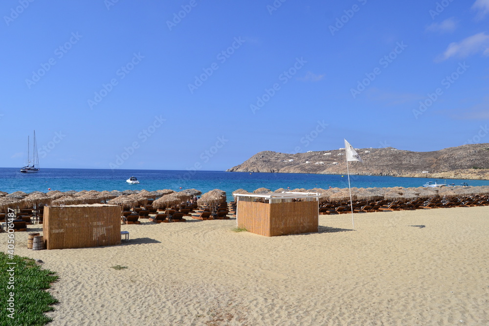 Beach in Mykonos with clear water, creating a gradient of blue and green with boat in the background Beach in Mykonos with clear water, creating a gradient of blue and green with boat in the background