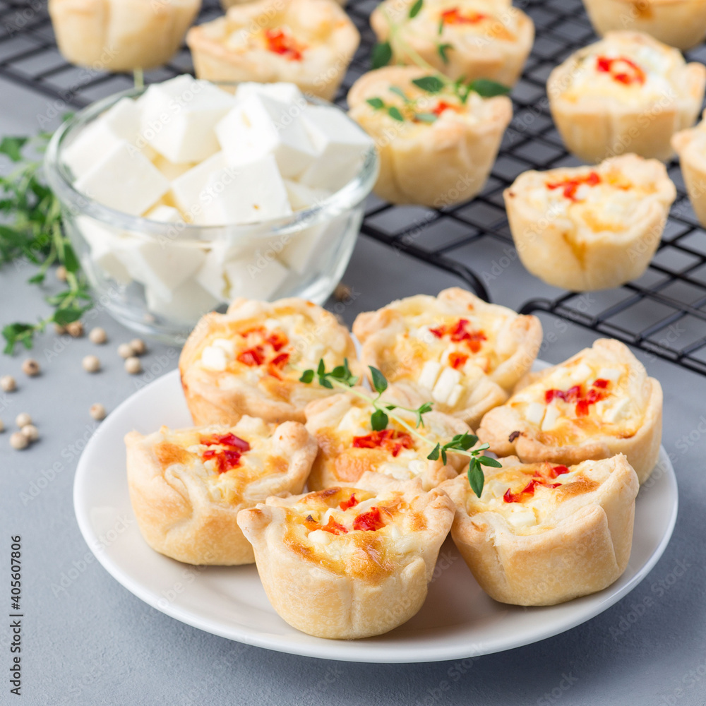 Feta cheese and fried onion mini quiche muffins, on white plate and cooling rack, square format