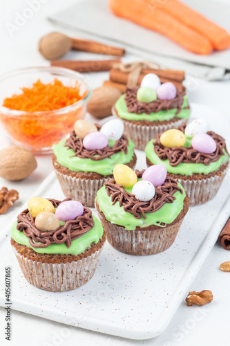 Homemade carrot cupcakes with cream cheese frosting and Easter chocolate eggs, on white plate, vertical
