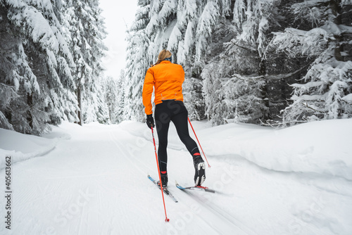 Langläufer von hinten mit orangener Jacke auf der Loipe im Winter