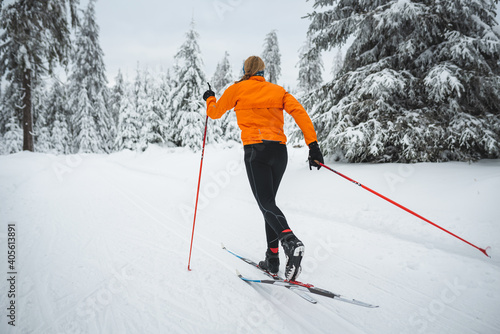 Bild auf Leinwand Langläufer von hinten mit orangener Jacke auf der Loipe im Winter