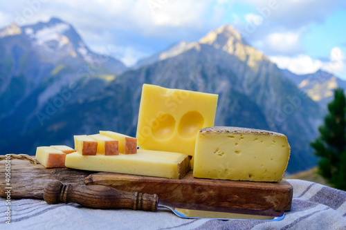 Cheese collection, French beaufort, abondance, emmental, tomme de savoie cheeses served outdoor in Savoy region, with Alpine mountains peaks on background photo