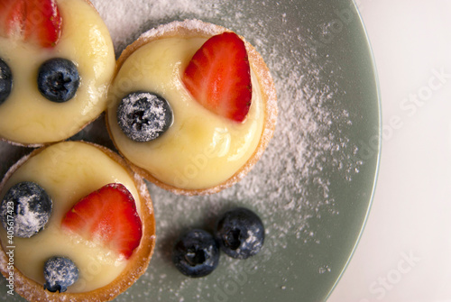 Top view of French dessert. Little tarts with custard, fresh berries and powdered sugar. Tartlets with strawberries, blueberries served with icing sugar on gray plate
 photo