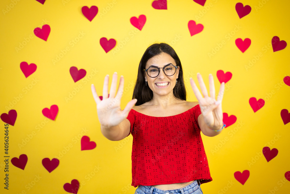 Young beautiful woman over yellow background with red hearts showing and pointing up with fingers number nine while smiling confident and happy Young beautiful woman over yellow background with red hearts showing and pointing up with fingers number nine while smiling confident and happy