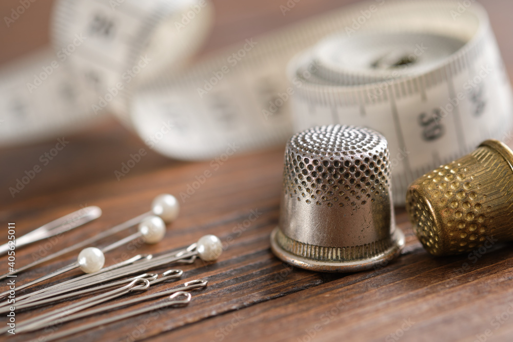 Sewing items - thimbles, including pins, measuring tape on background. - obrazy, fototapety, plakaty 