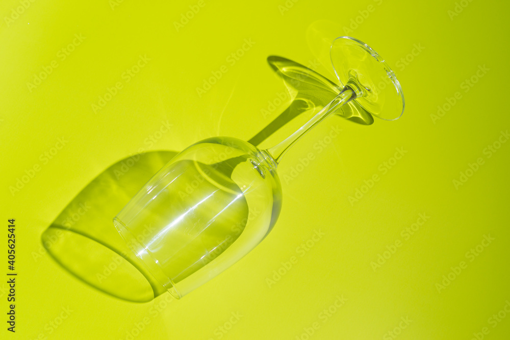 Wine glass lies on lemon green background. 