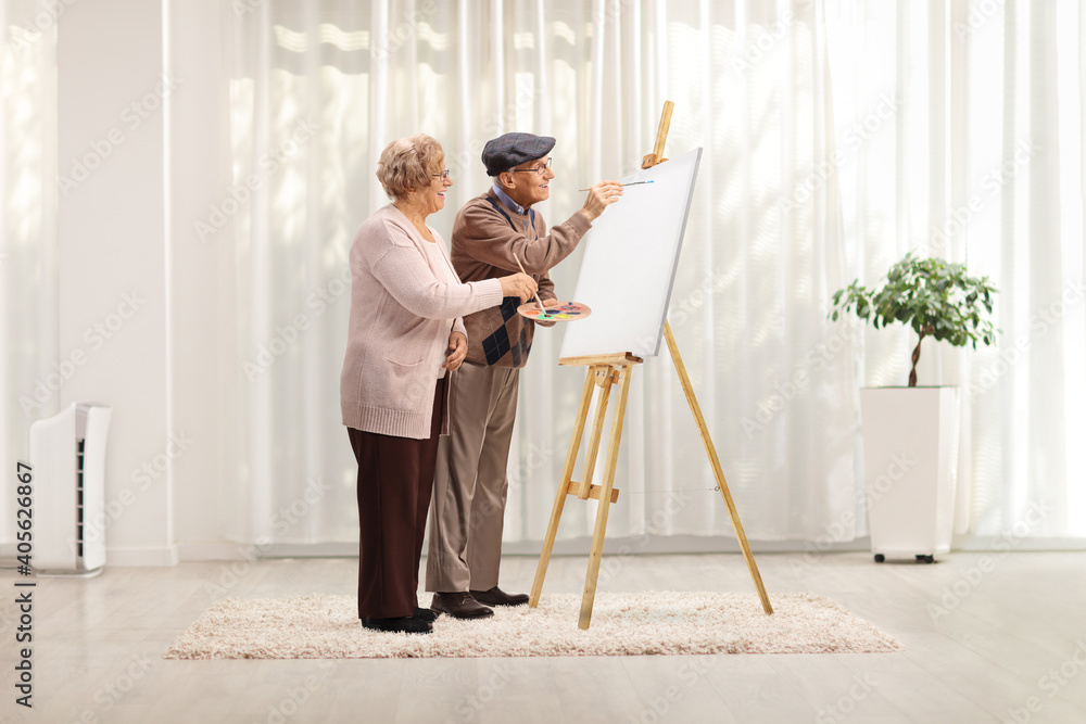 Elderly couple painting with brushes on a canvas at home