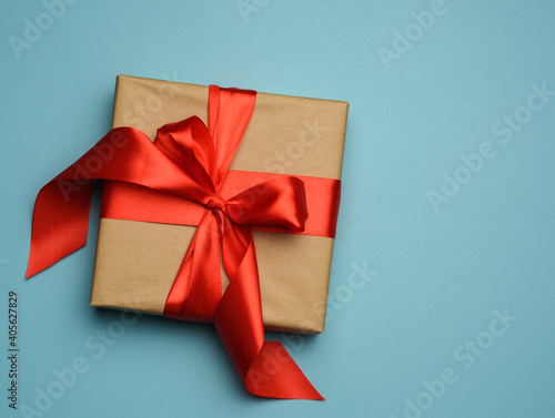 square gift box is packed in red paper and curled red silk ribbon, festive background