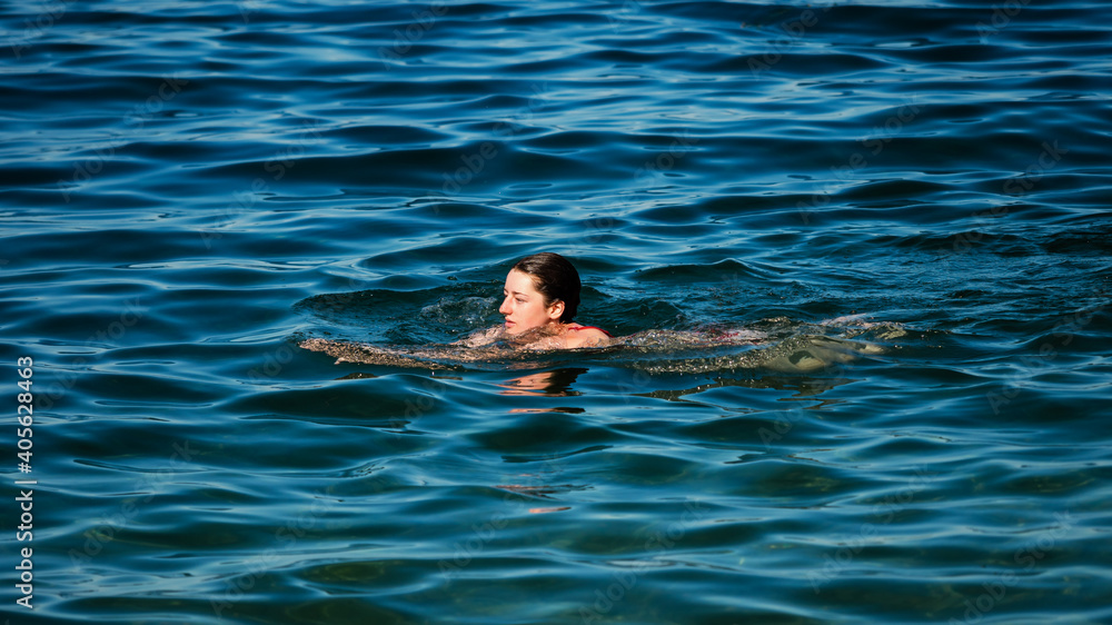 A young girl swims in the crystal clear water of a mountain lake.