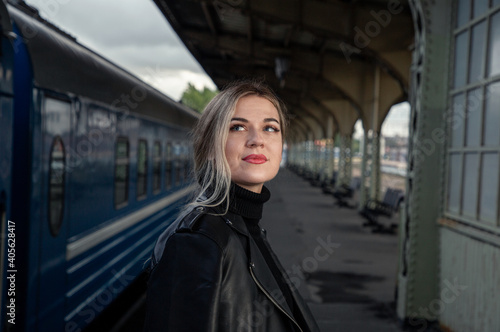 Portrait of a young beautiful woman in a leather jacket on a perone next to the train at the railway station. Waiting for the train Vitebsk station St. Petersburg.