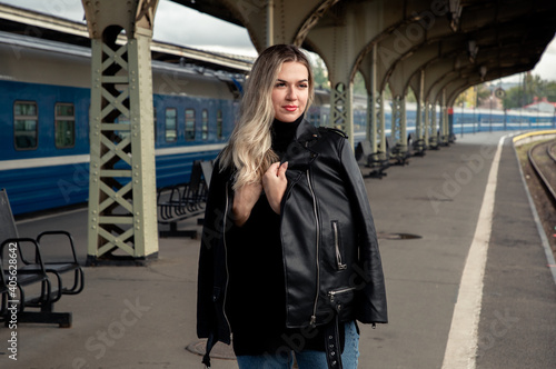 Portrait of a young beautiful woman in a leather jacket on a perone next to the train at the railway station. Waiting for the train Vitebsk station St. Petersburg.