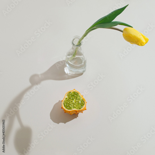 Yellow flower tulip in the glass bottle and kawani fruit against gray background. photo