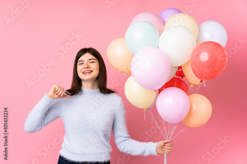 Young Ukrainian teenager girl holding lots of balloons over isolated pink background proud and self-satisfied