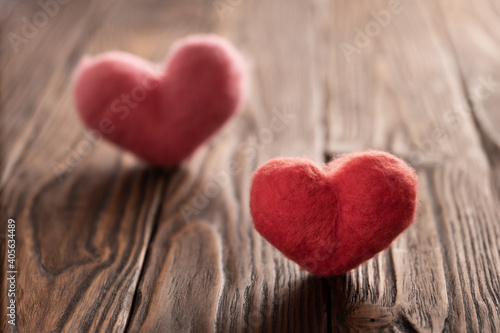 Two woolen backlit handmade hearts stand on the brown textured wooden boards. Valentine s day concept.