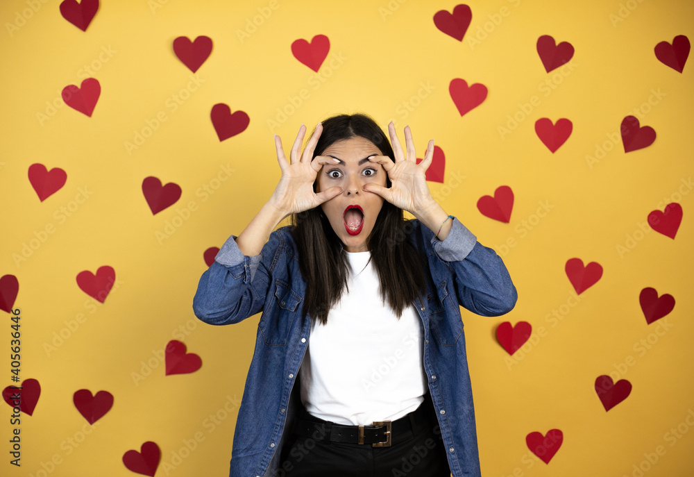Young caucasian woman over yellow background with red hearts Trying to open eyes with fingers, sleepy and tired for morning fatigue Young caucasian woman over yellow background with red hearts Trying to open eyes with fingers, sleepy and tired for morning fatigue