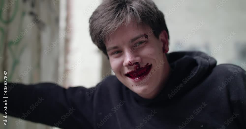 Bloodied man laughing at camera and suffering from pain in an abandoned building Bloodied man laughing at camera and suffering from pain in an abandoned building