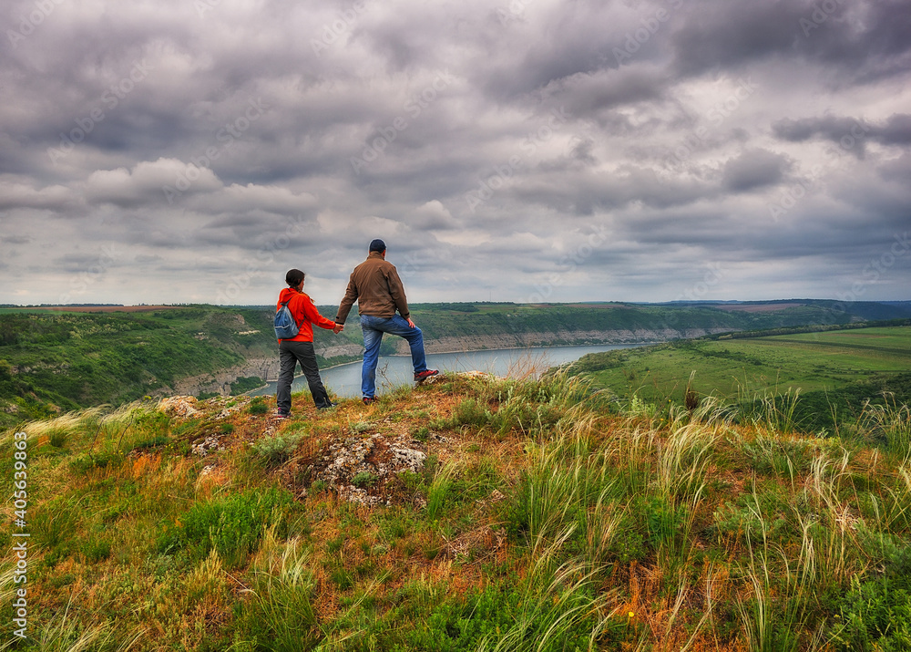 couple of tourists on the rock. a man and a woman look at the picturesque river canyon couple of tourists on the rock. a man and a woman look at the picturesque river canyon