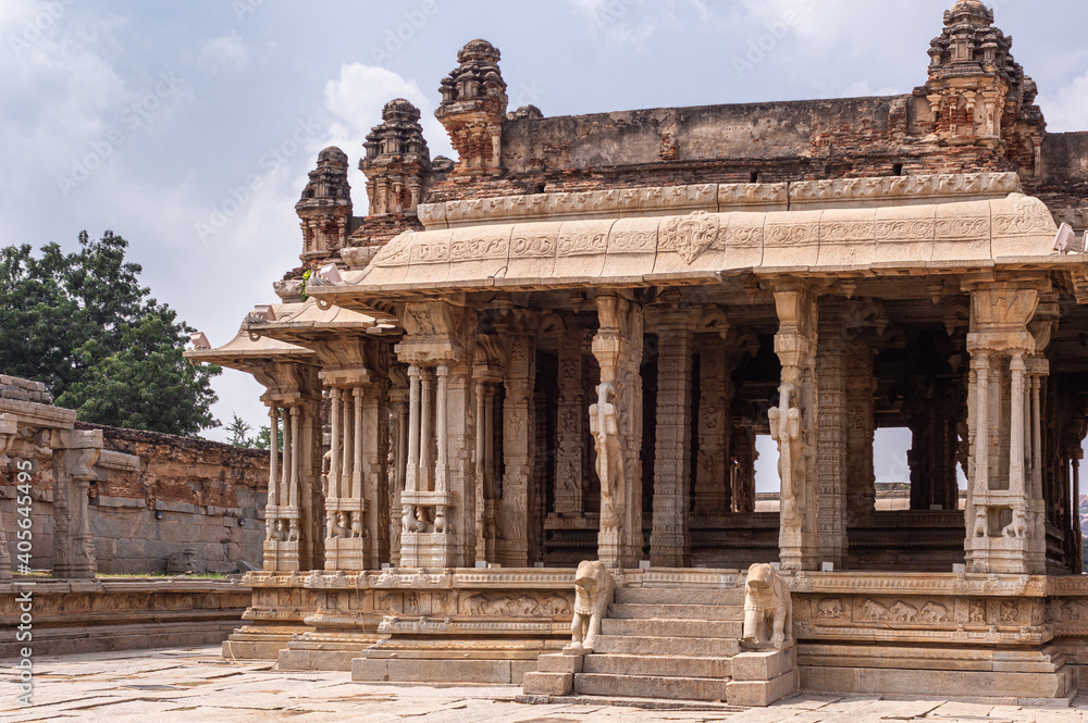 Hampi, Karnataka, India - November 5, 2013: Vijaya Vitthala Temple. Entrance with beige sculpted pillars and steps to ruinous mandapam of sanctuary. Horse and elephant statues.