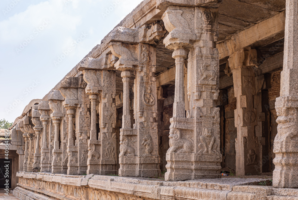 Hampi, Karnataka, India - November 5, 2013: Vijaya Vitthala Temple. Beige stone row of sculpted pillars along wall under light blue sky. Narasimha frescos galore.