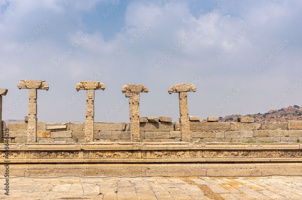 Fototapeta premium Hampi, Karnataka, India - November 5, 2013: Vijaya Vitthala Temple. Remains of brown stone wall pillars with missing roof under blue cloudscape,