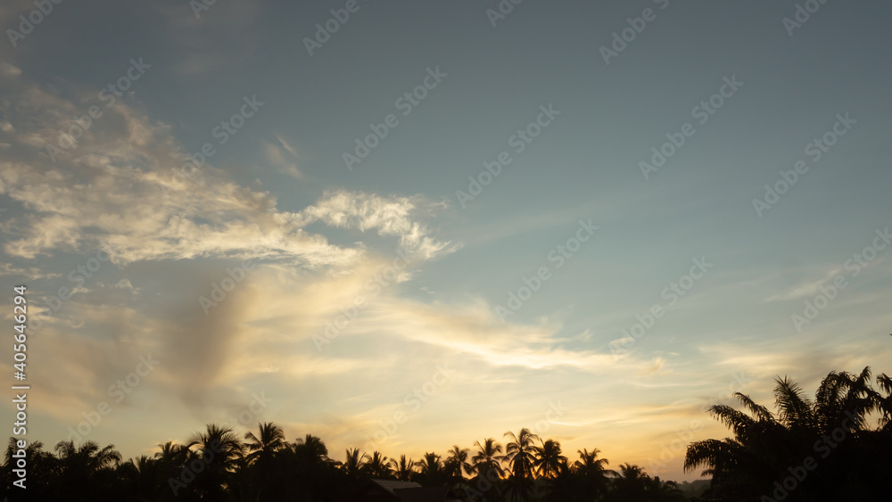 TimeLapse of first light dawn time, color of morning, flares shining through coconut trees on beautiful blue sky background, wispy clouds bluds up vertical line, sunrise at silhouette palm trees.