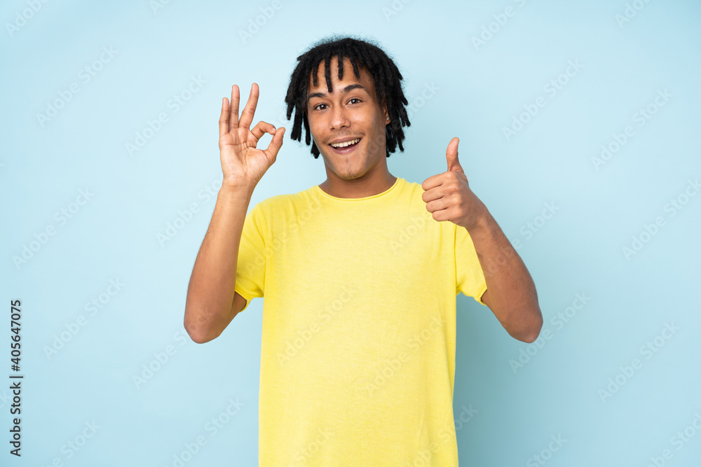 Young african american man isolated on blue background showing ok sign and thumb up gesture Young african american man isolated on blue background showing ok sign and thumb up gesture